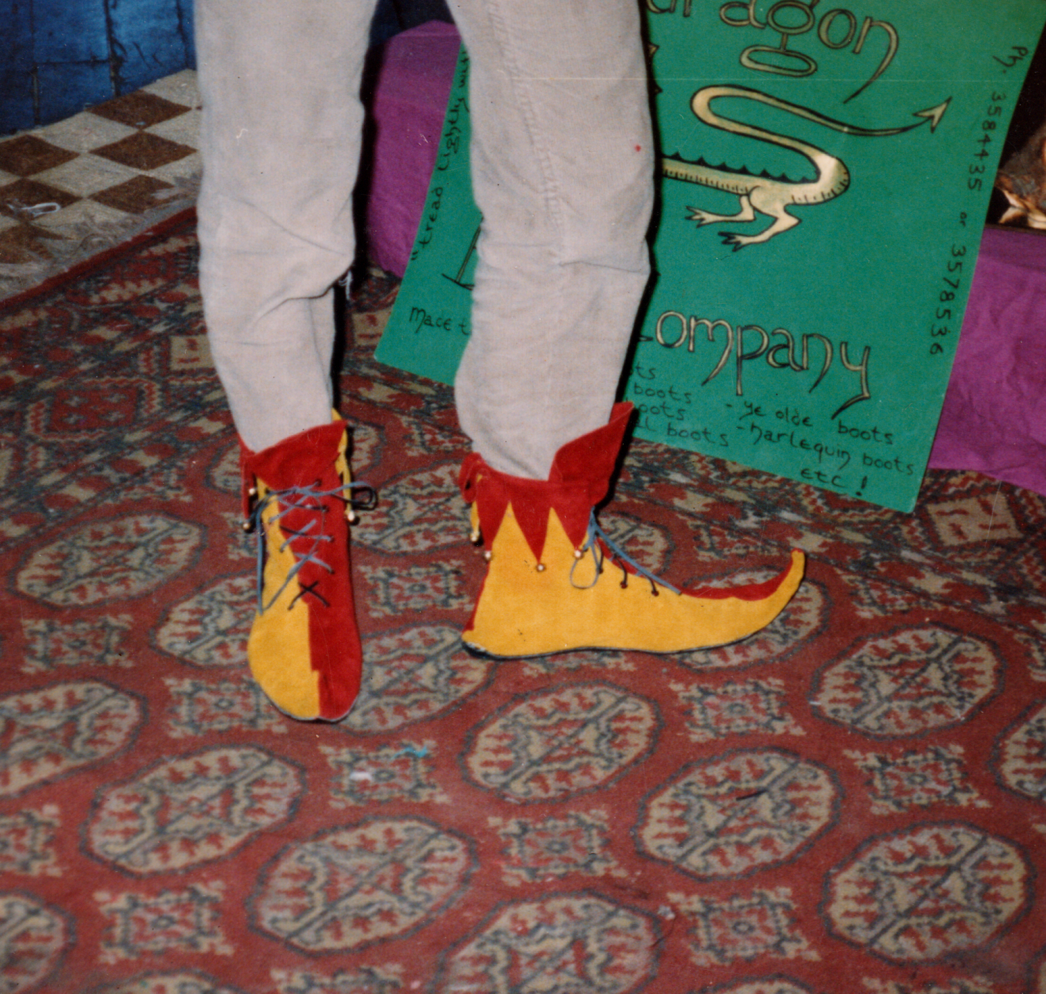 Colorful pair of costume shoes that look like a cowboys or clowns, placed on a patterned red and blue carpet.
