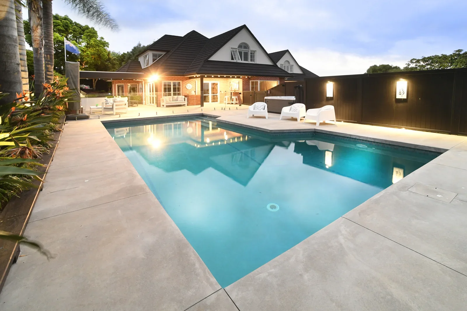Concrete pool surround beside a contemporary home at dusk
