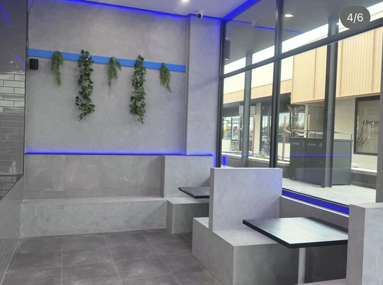 Modern interior with gray tiled bench seating, wall-mounted greenery, and blue LED lighting accents near large glass windows.