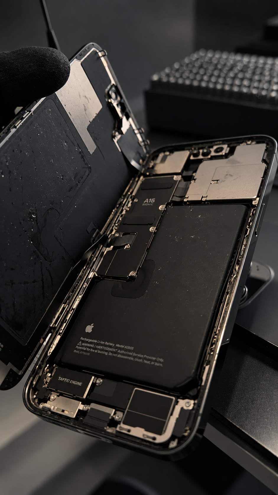 Un teléfono inteligente de tipo iPhone abierto revelando su interior, incluyendo la batería, componentes electrónicos y cables, en un entorno de reparación.