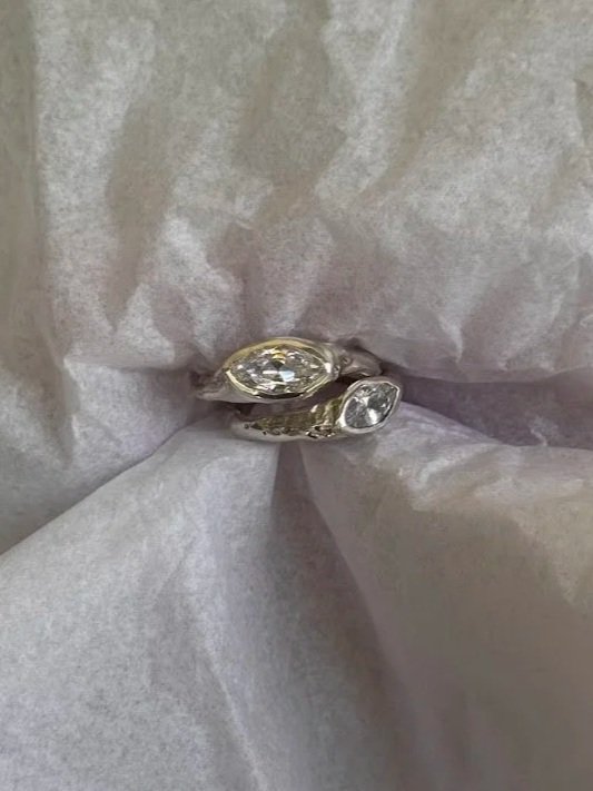 Two rings, one with a large oval gemstone and the other a smaller round gemstone, are placed together on crumpled tissue paper.