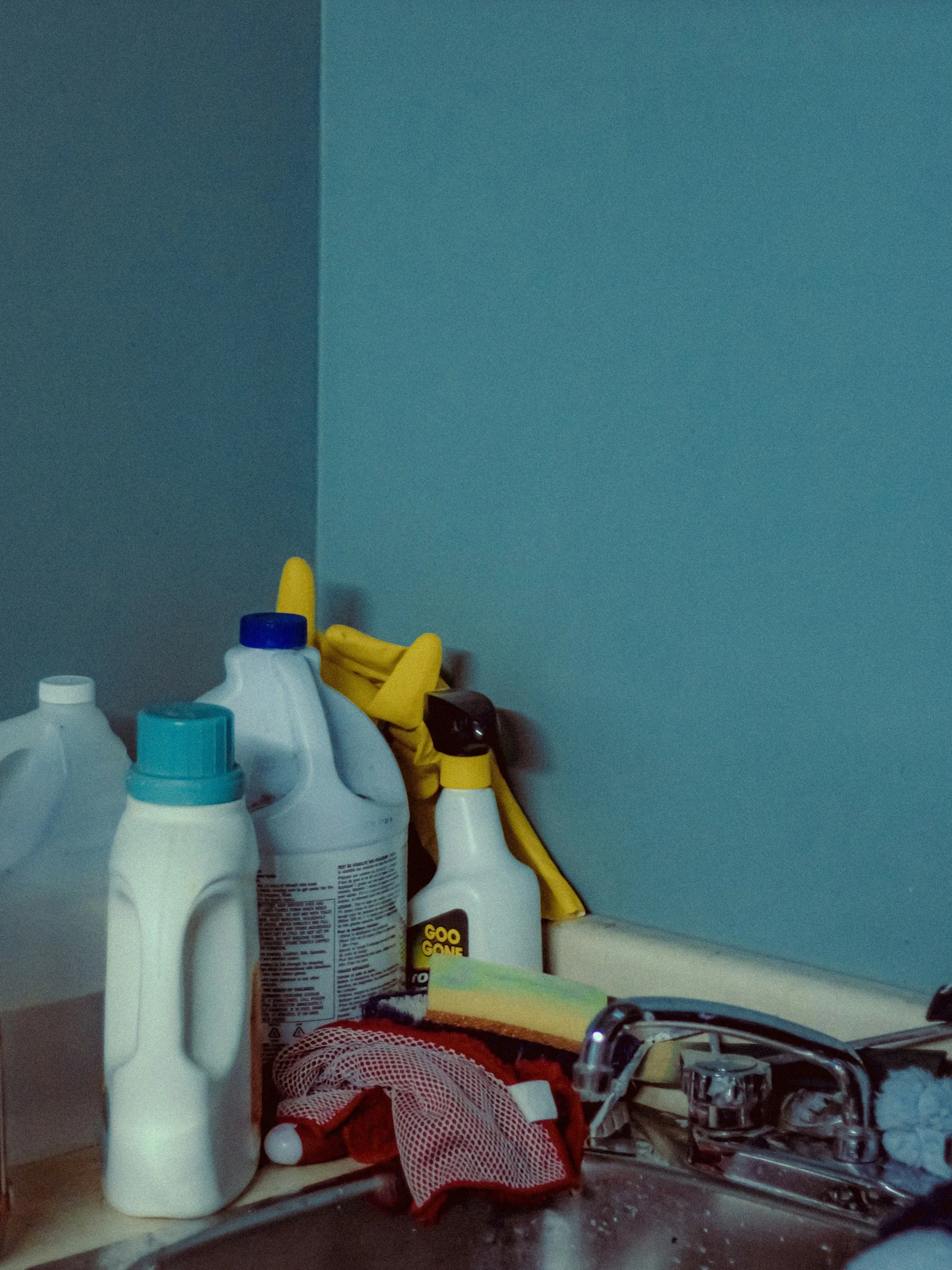 Cleaning supplies, yellow rubber gloves, sponge, dishcloth, and spray bottles beside a kitchen sink