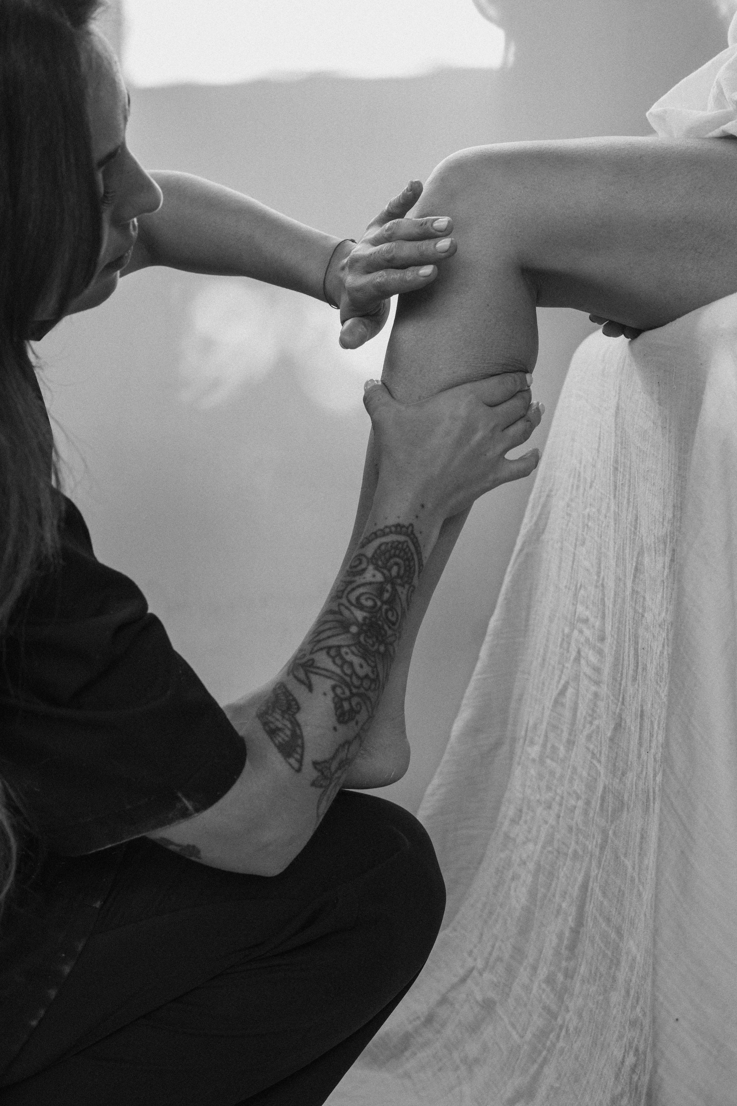 Une femme tatouée aidant une autre personne à faire de l'exercice de musculation, appui sur l'épaule de cette personne.