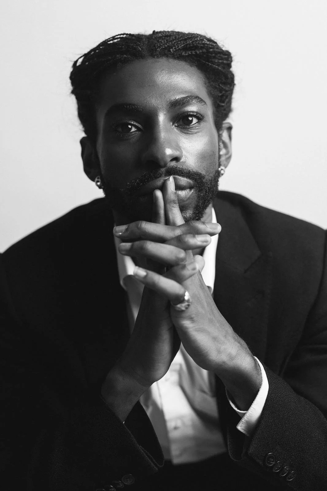 Black-and-white portrait of Emmanuel Diela Nkita in a suit holding his fingers to his lips in a quiet gesture