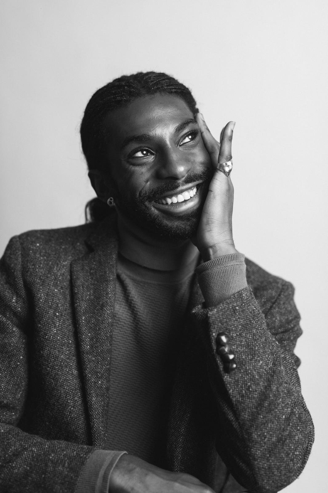 Black-and-white portrait of Emmanuel Diela Nkita wearing a blazer and resting his face on his hand