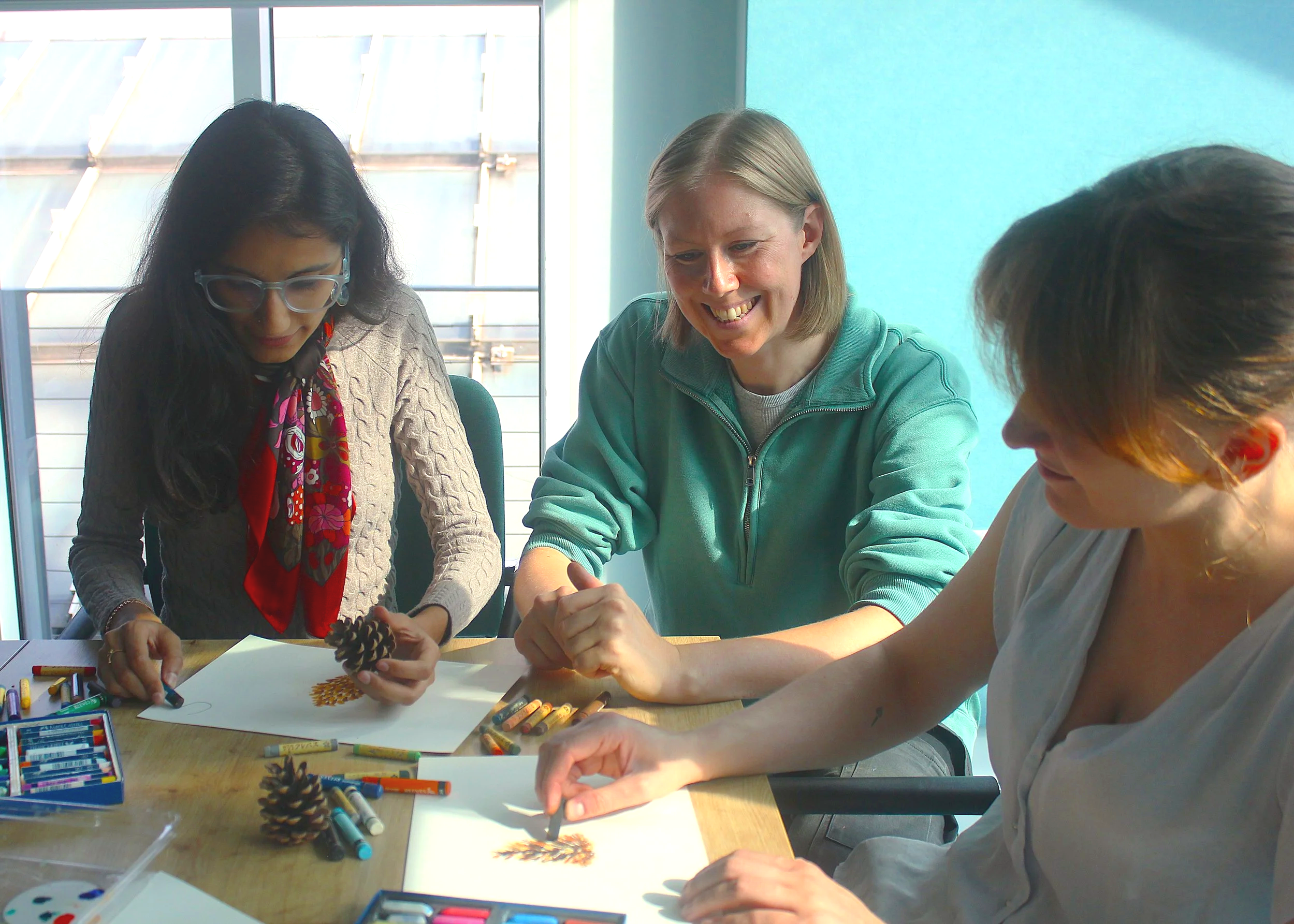 People in and office sitting at a table sketcing pine cones