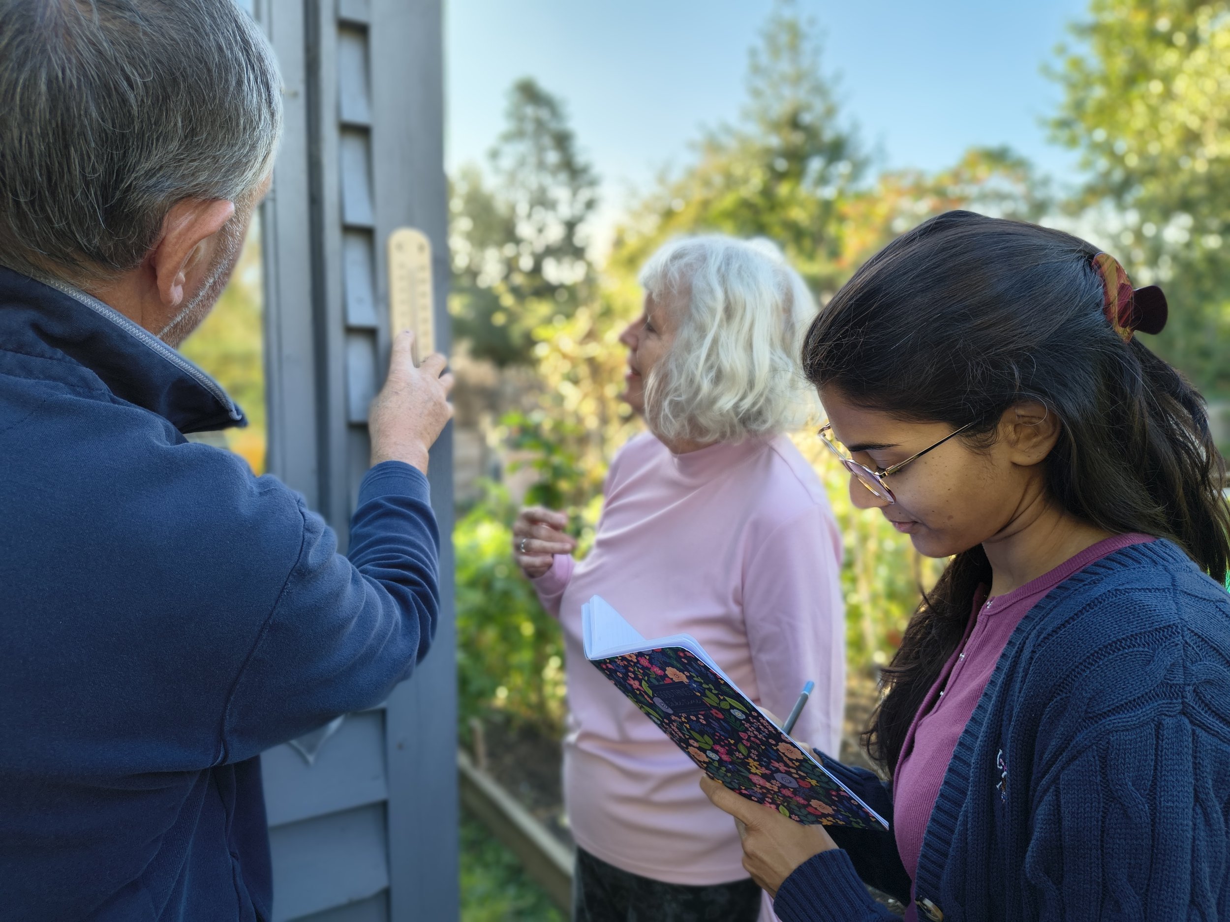 A group of three people in a garden looking at a thermometer
