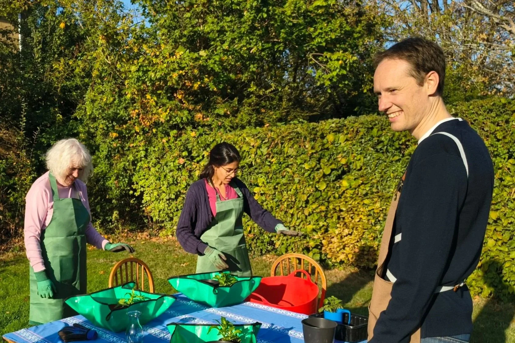 Three people in a garden potting plants at a table