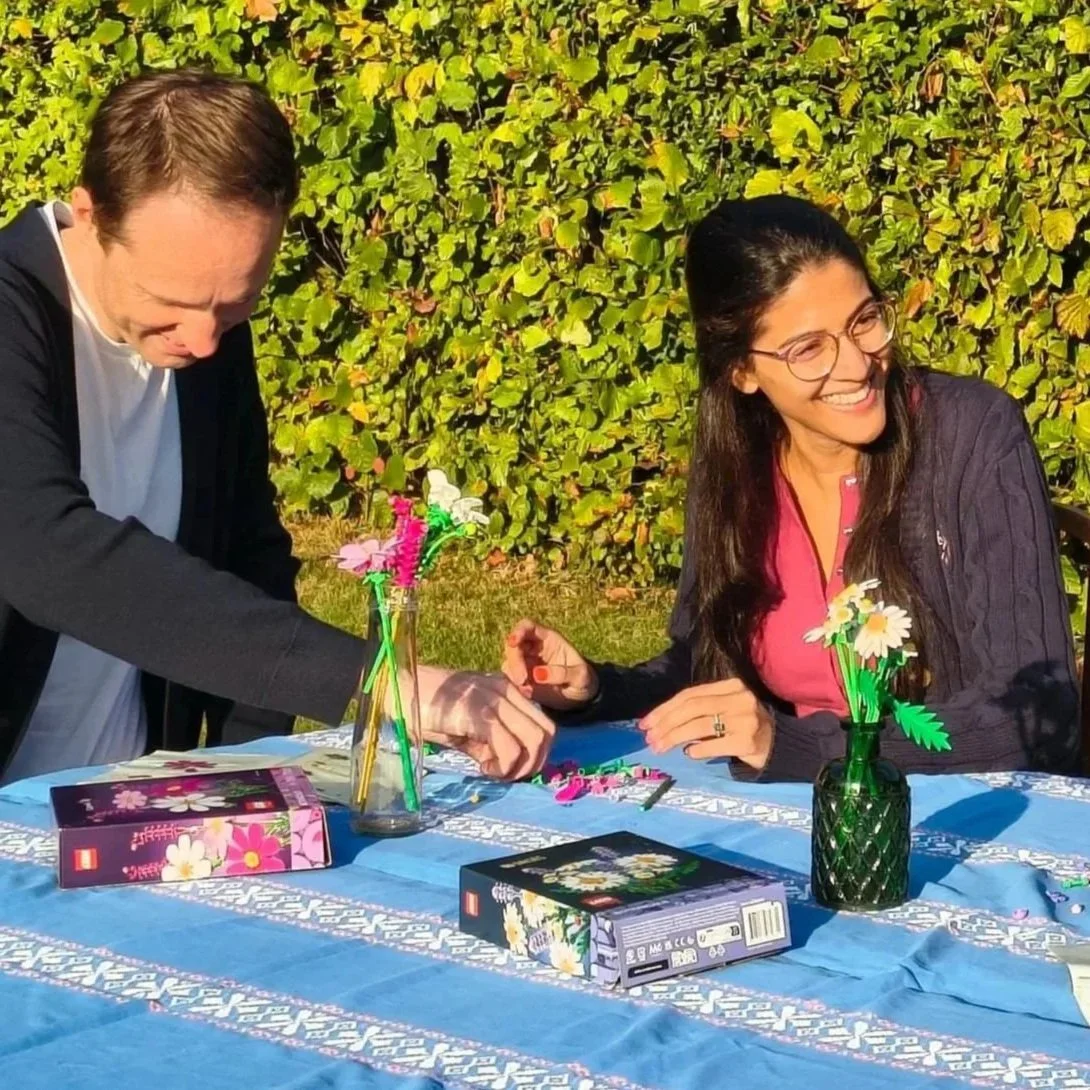 Two people sitting at a table in a garden making Lego flowers
