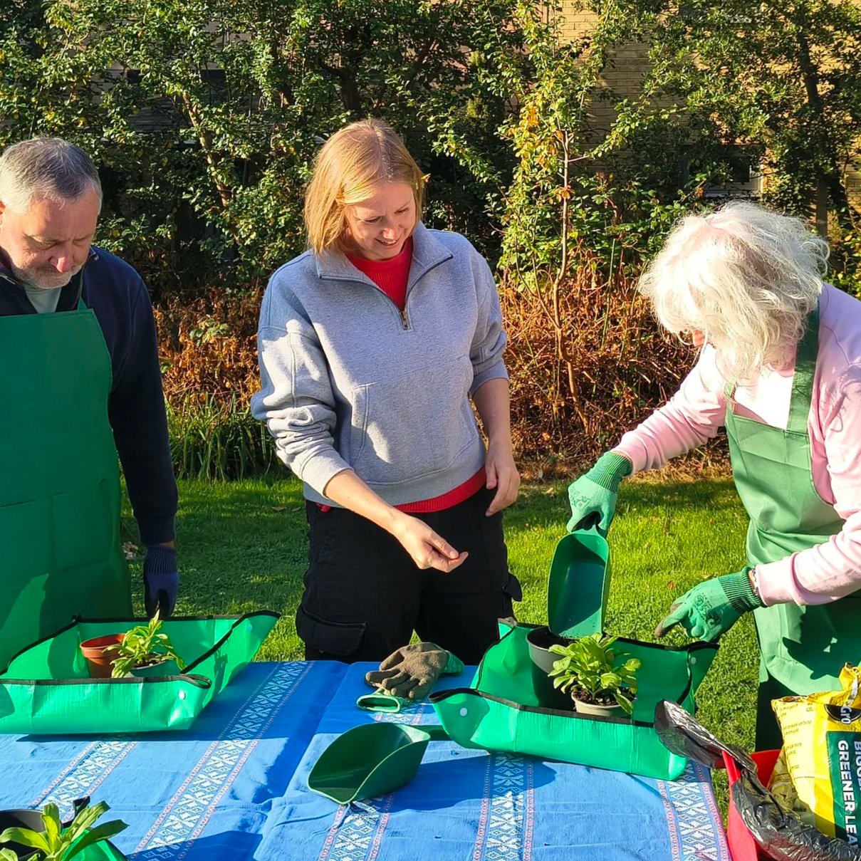 People potting plants at a table in a garden