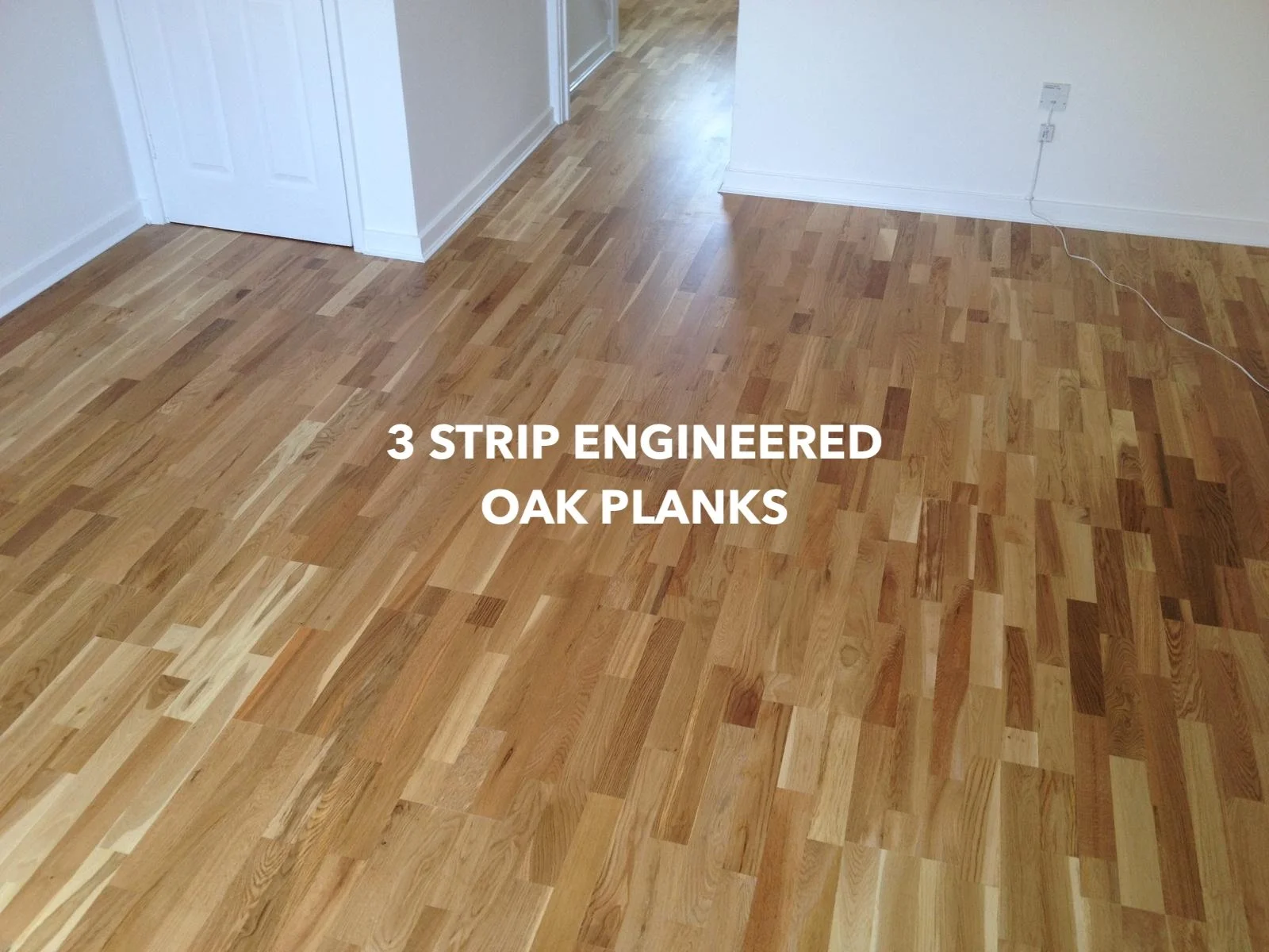 Three-strip engineered oak plank flooring leading through a doorway.