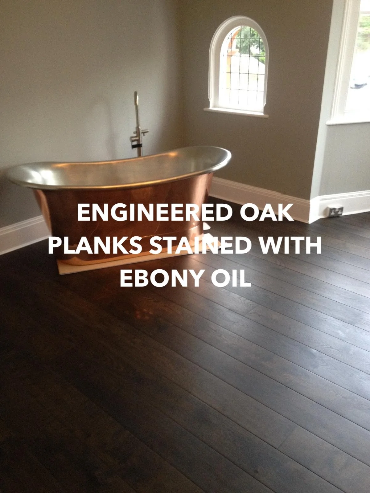 Ebony-oiled engineered oak floor planks beneath a freestanding copper bath.