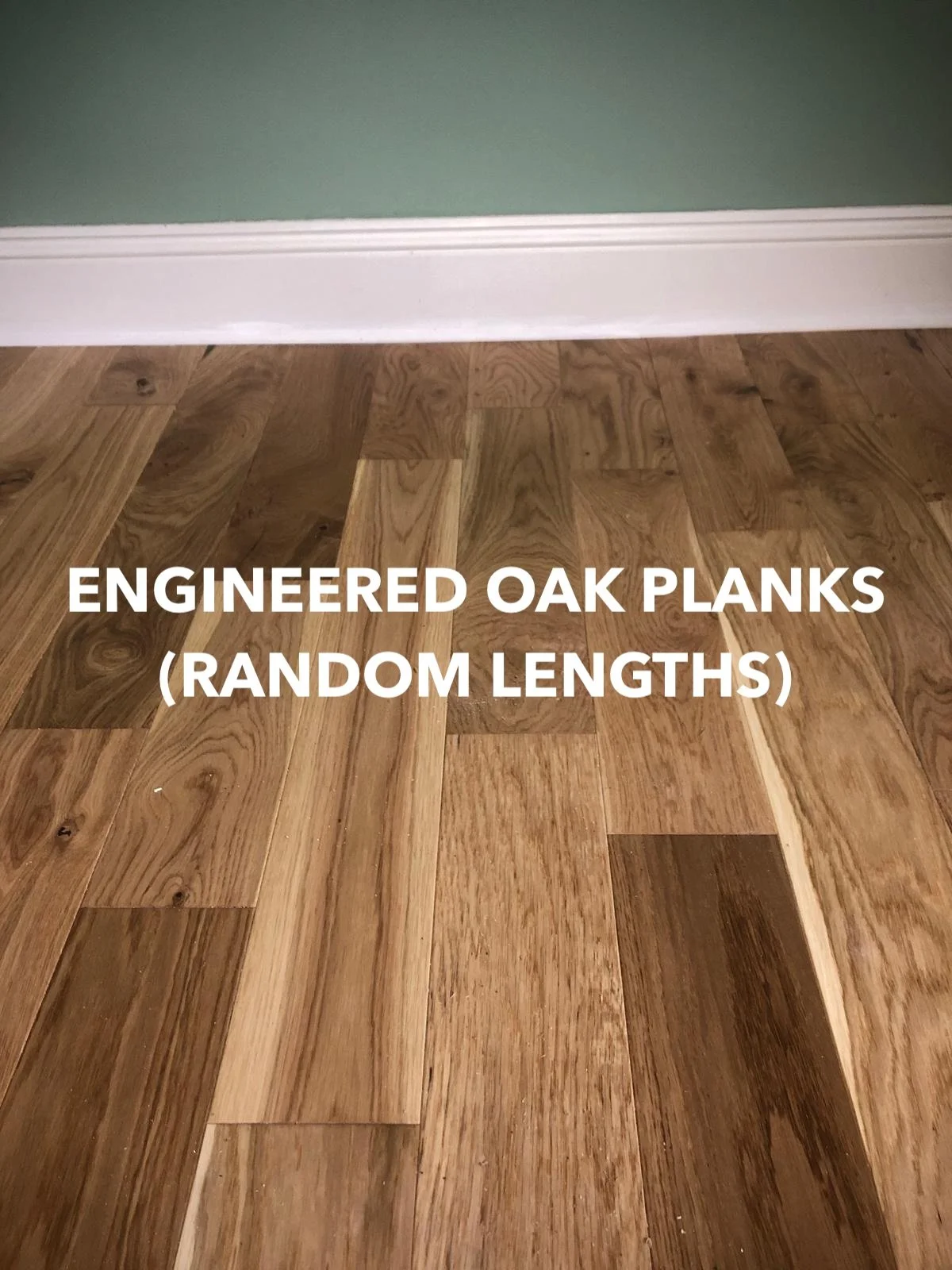 Random-length engineered oak planks beside a green wall and white skirting.