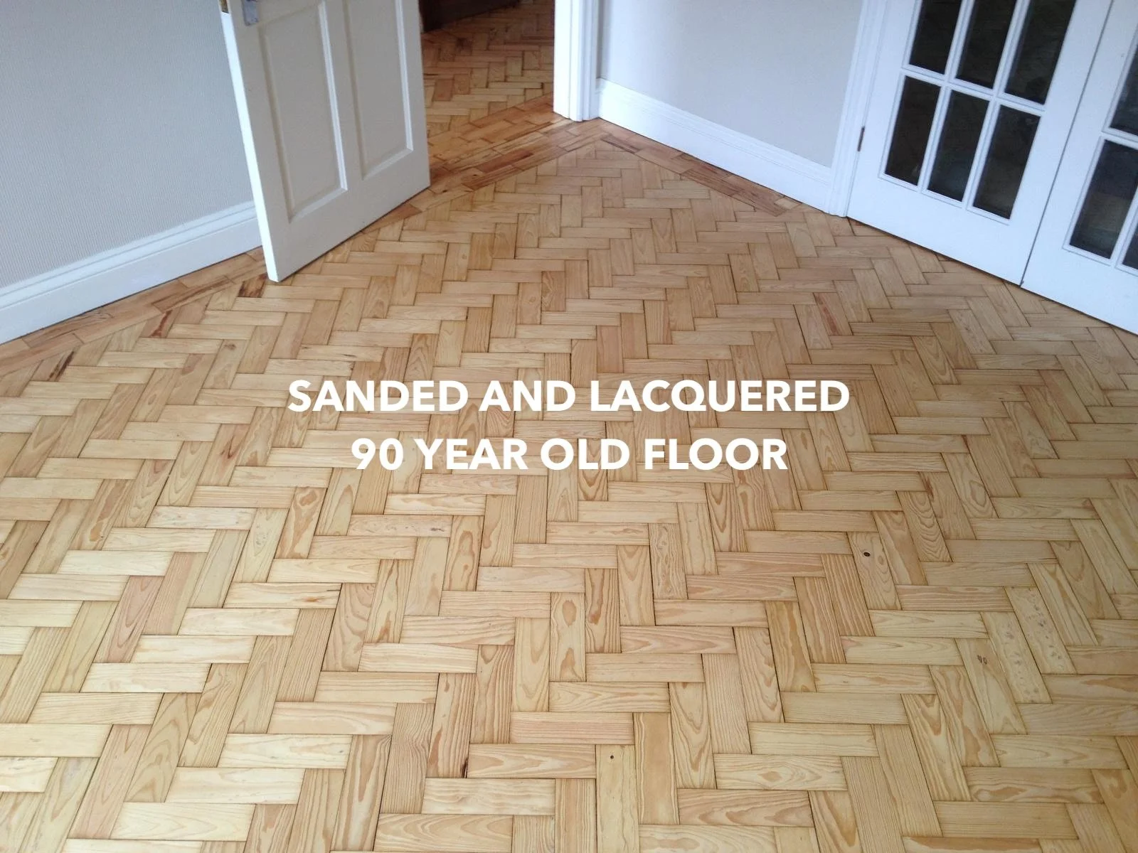 Sanded and lacquered herringbone wood floor beside glazed double doors.