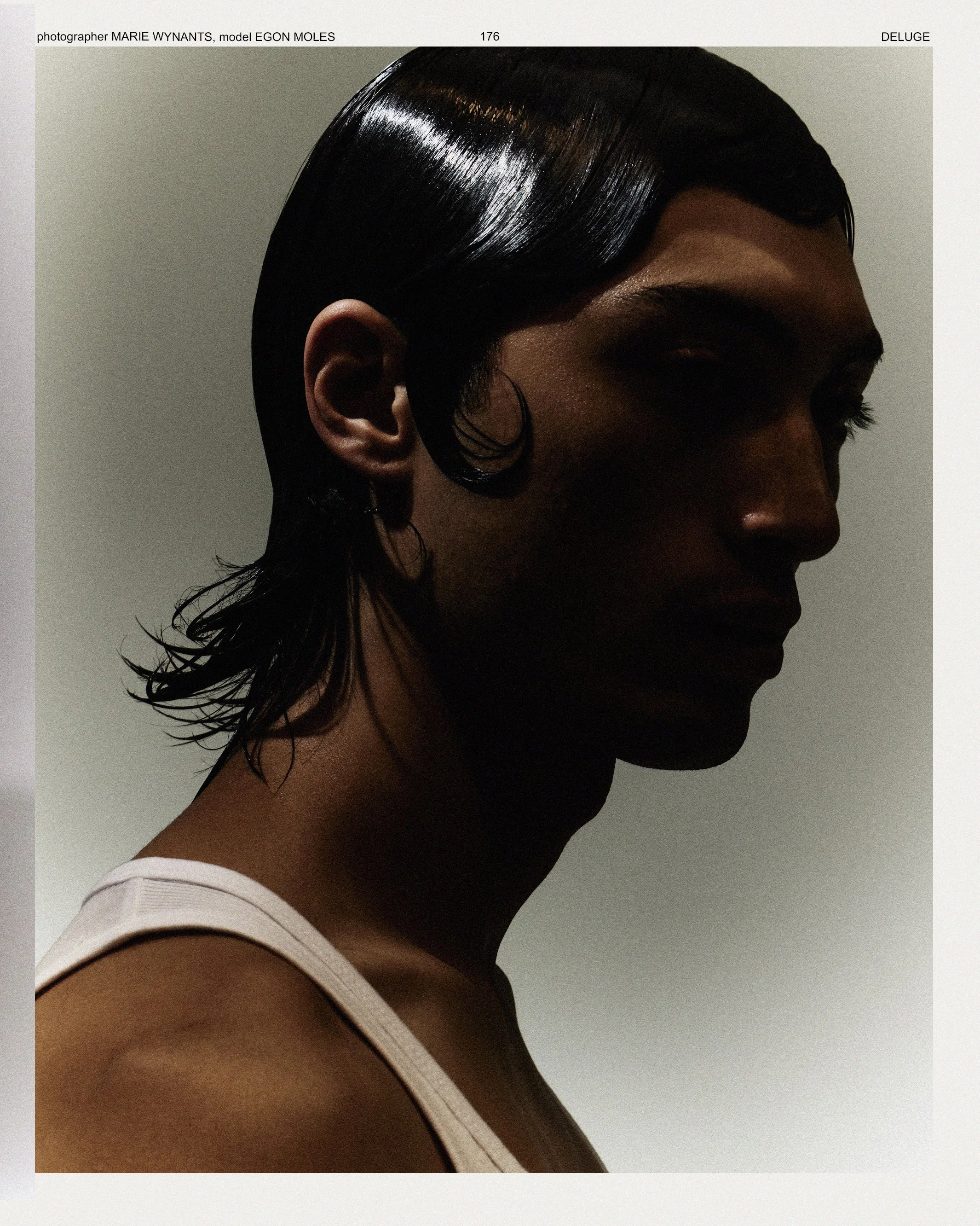 Close-up side profile of a woman with dark, shiny, straight hair, wearing hoop earrings and a white top, against a plain background.