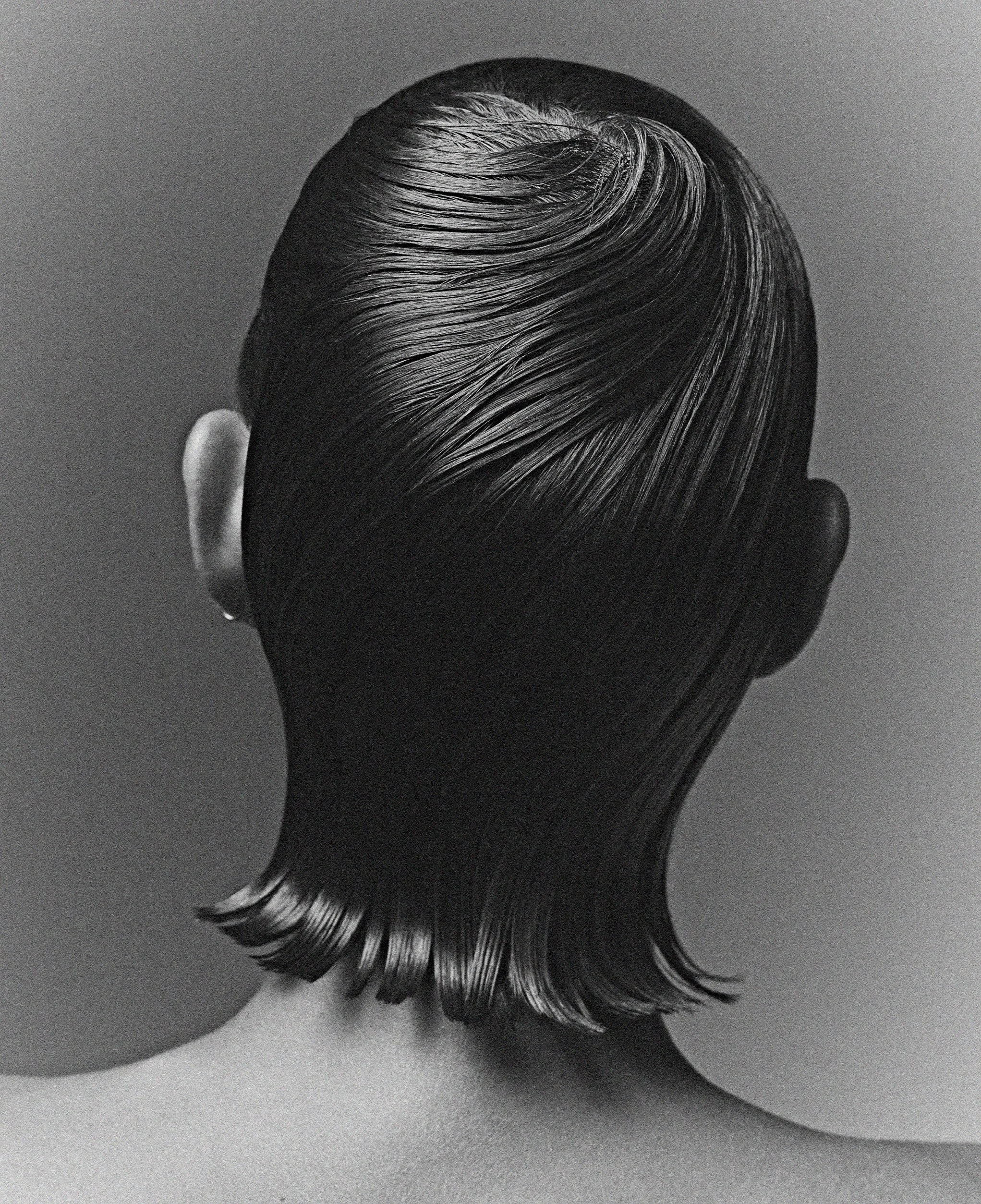 Close-up of a person's head with short, dark, neatly styled hair, alongside two large round objects on a light surface.