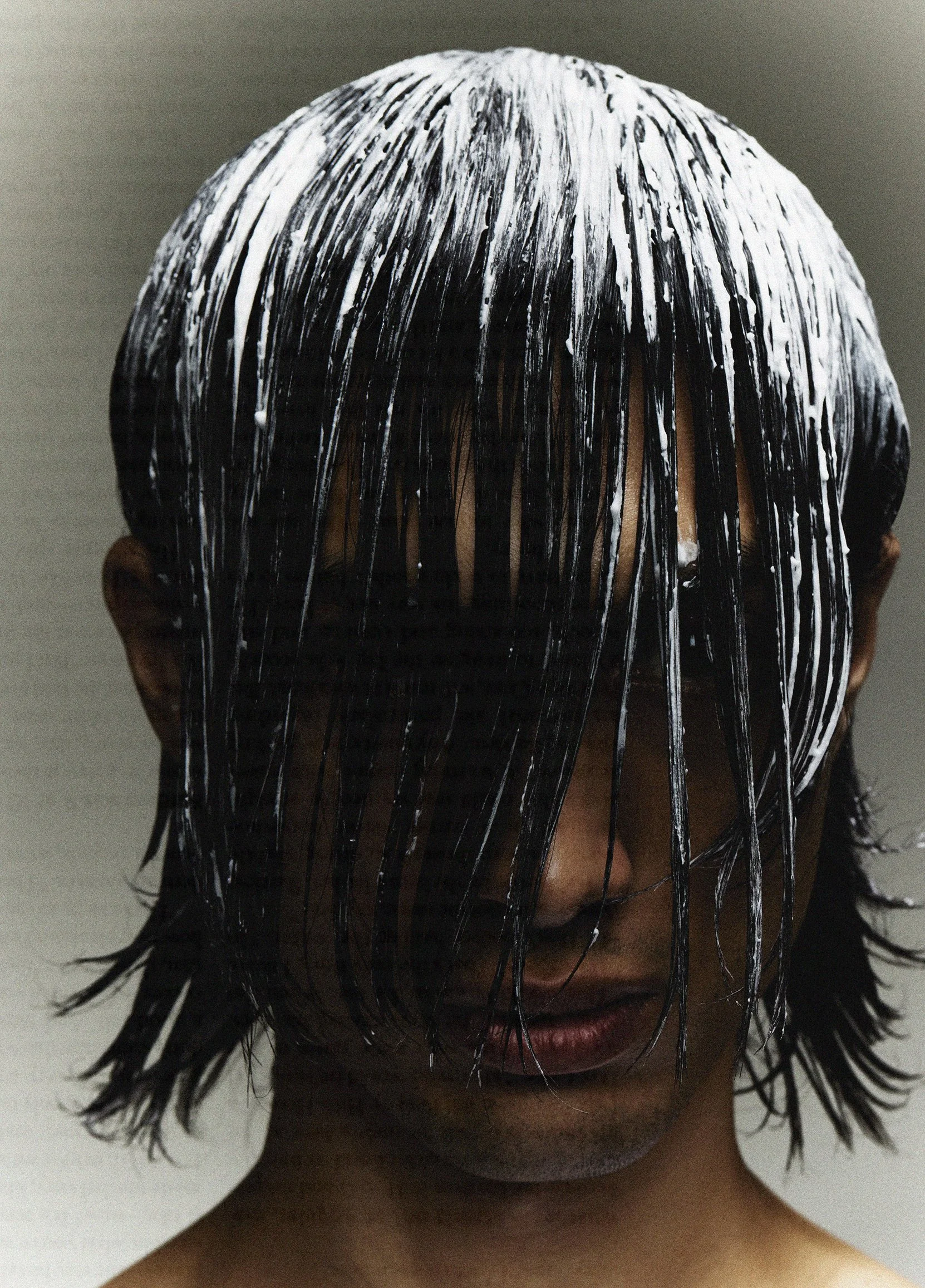 A person with wet, black hair covered in white paint drips, obscuring their face.