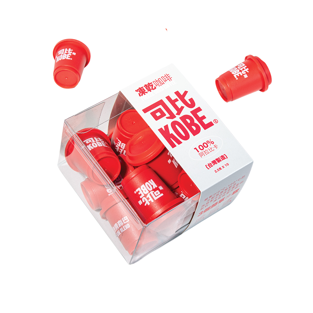 Red capsule-shaped containers with white text that says 'KOBE' and Japanese characters, scattered on a white surface with a clear plastic container and a printed sign with red Japanese characters and English text.