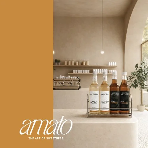 Display of bottled syrups on a countertop in a minimalist cafe with shelving and plants in the background.