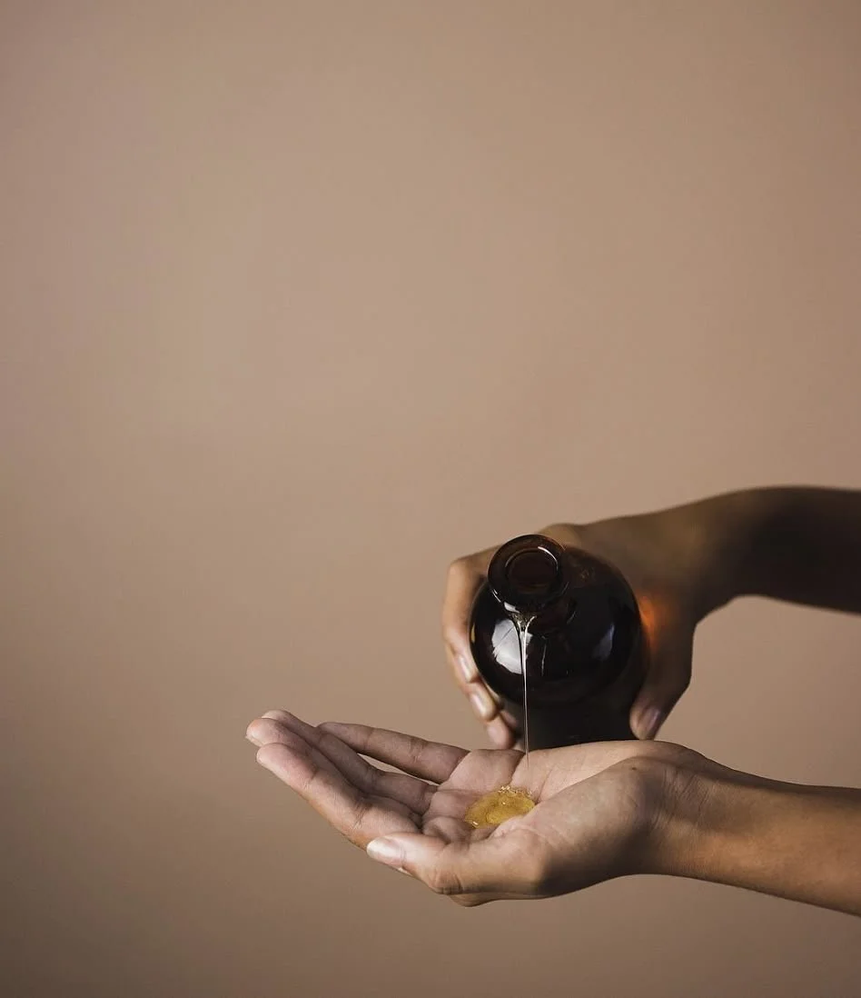 Person pouring a liquid from a brown bottle into their open palm against a plain neutral background.