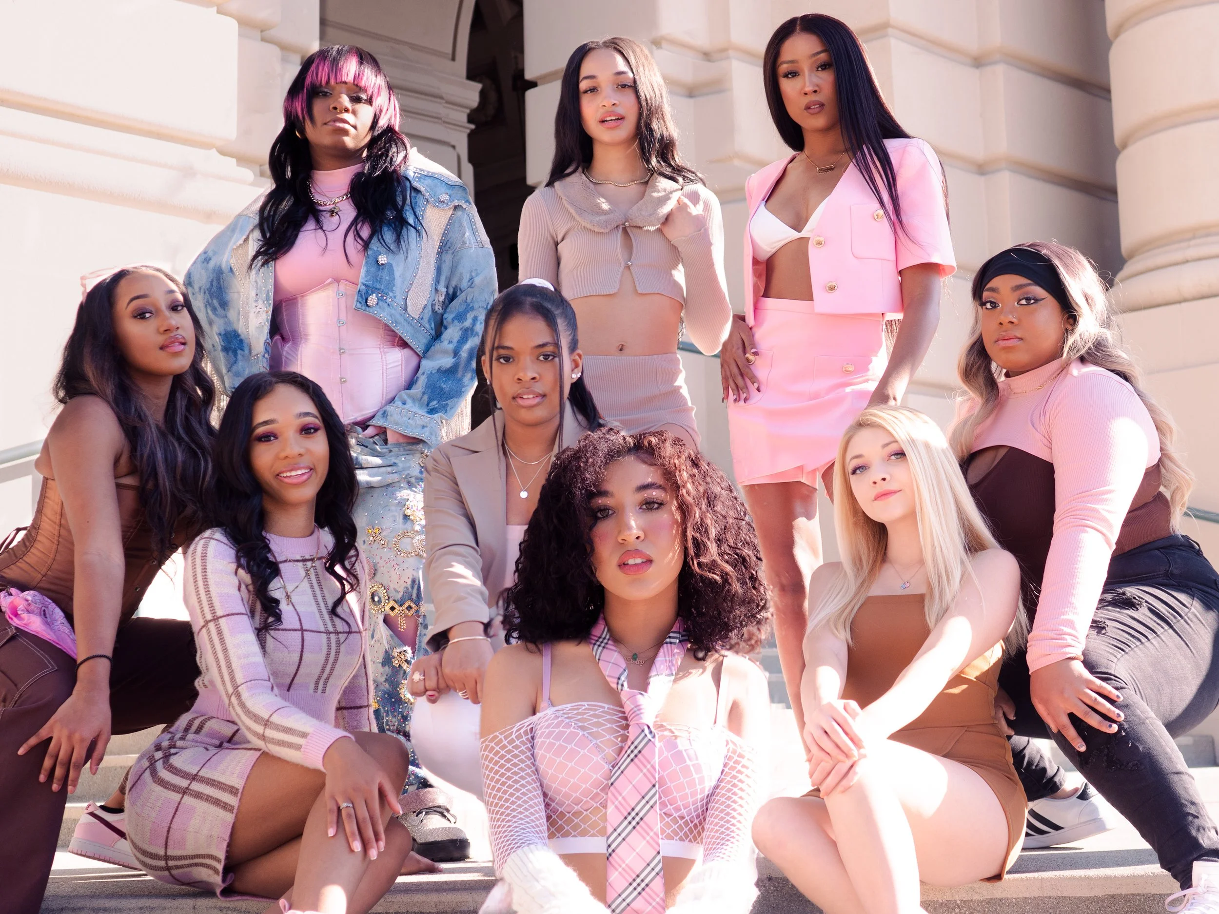 A diverse group of ten young women posing on the steps of a building, dressed in colorful stylish fashion.
