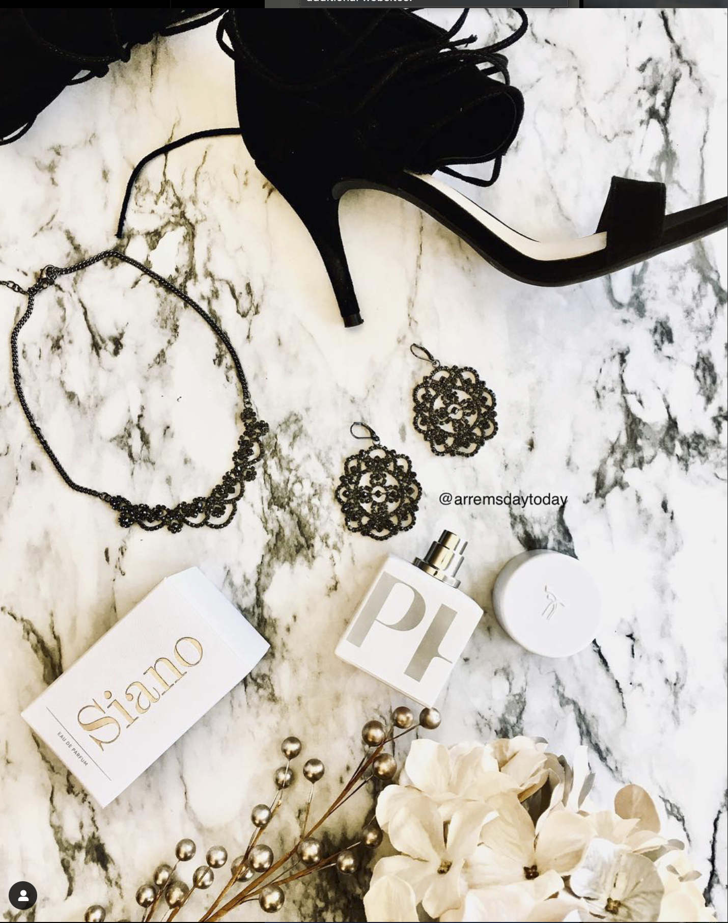 Black high-heeled sandal, black jewelry set including necklace and earrings, white perfume bottles, a white box labeled 'Siano', dried flowers, and white hydrangea flowers on a marble surface.