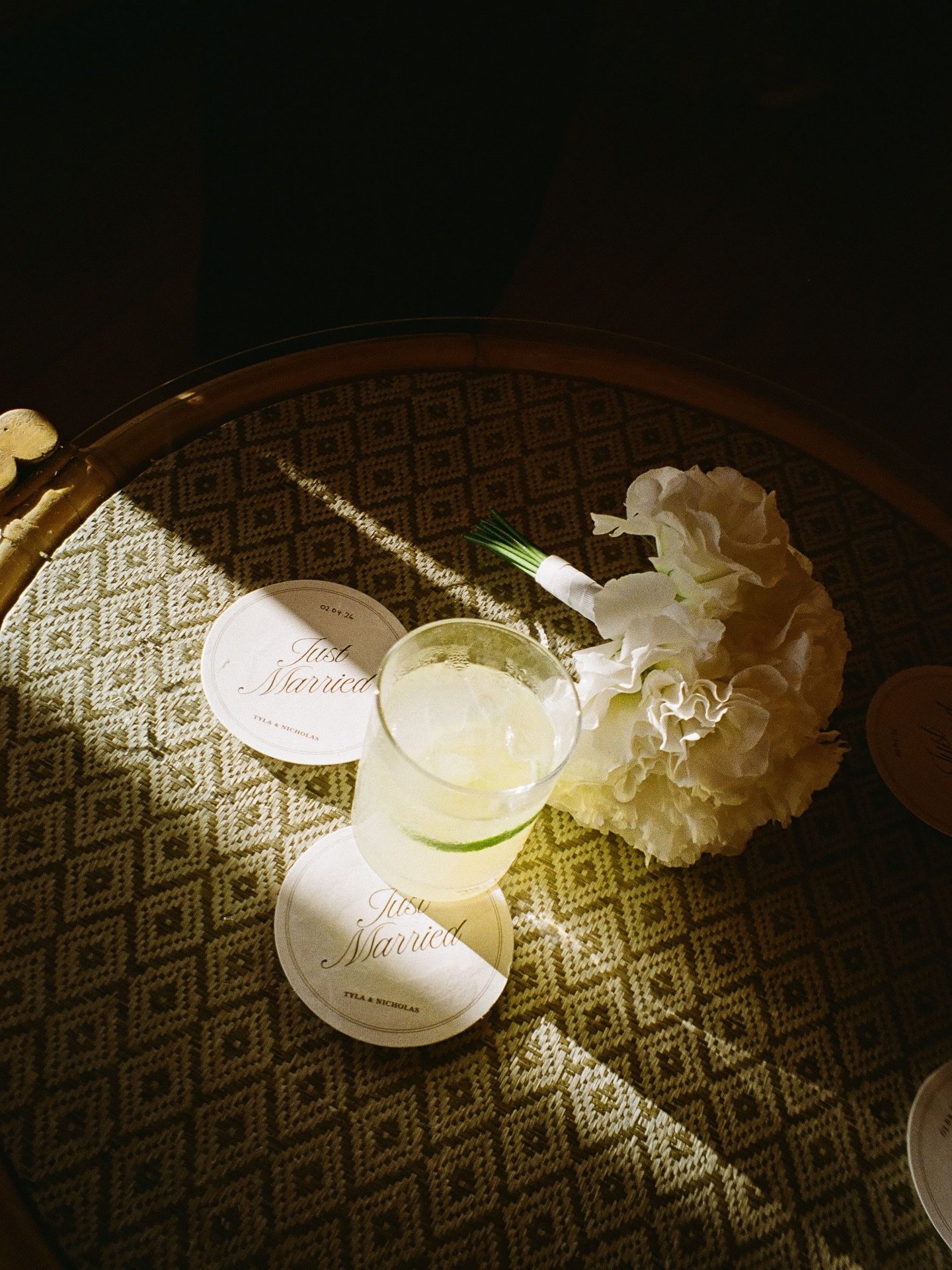 A wedding table setting with a 'Just Married' sign, a bouquet of white flowers, and a glass of beverage on a patterned tablecloth.