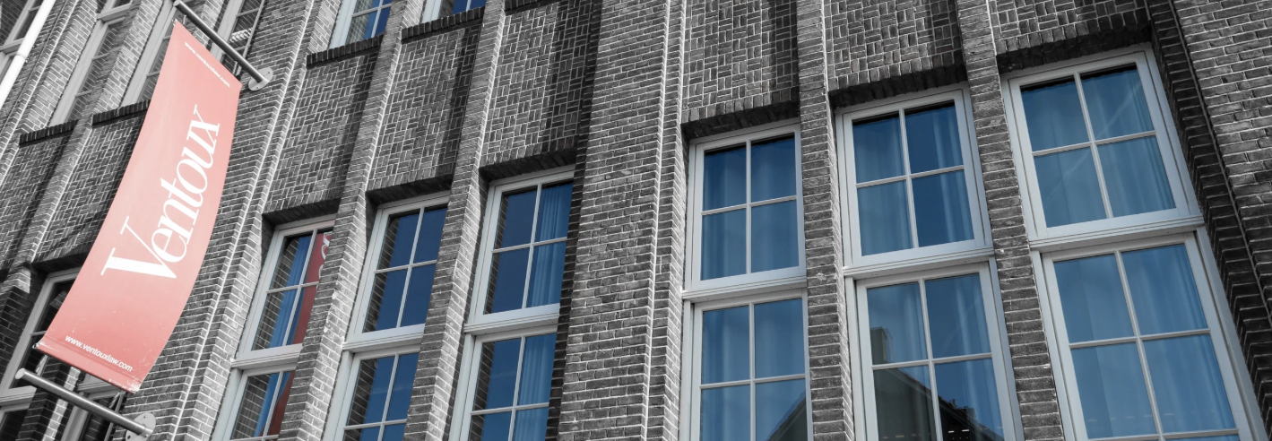 Exterior of a brick building with multiple windows and a pink banner that reads 'Venture' and includes a website URL.