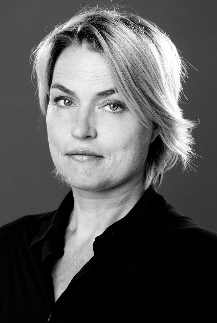Black and white portrait of a woman with short, tousled hair, wearing a dark shirt, looking directly at the camera with a confident expression.