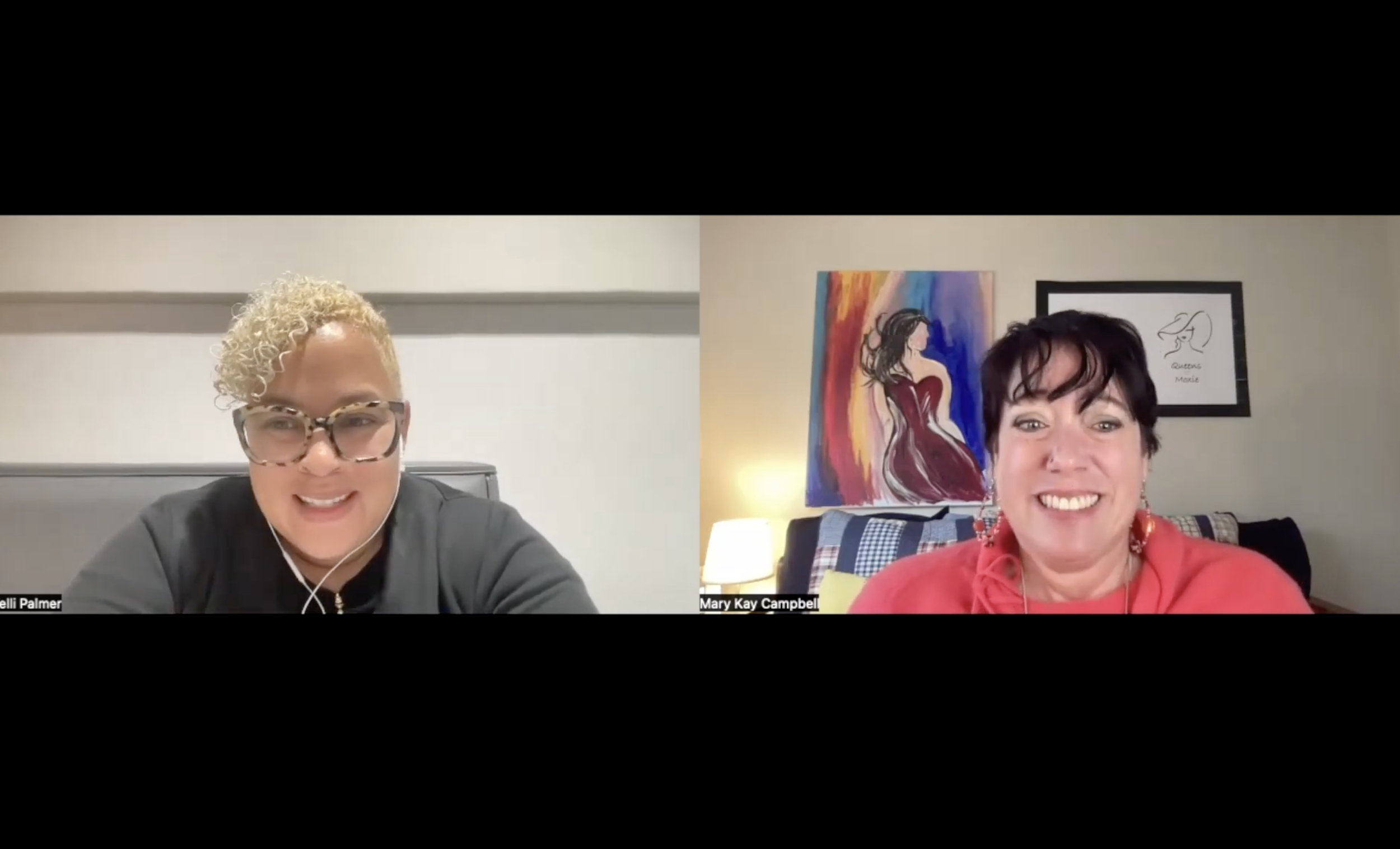 Two women smiling during a video call, one with curly blond hair and glasses, the other with short dark hair and a red top, in a room with framed artwork on the wall.