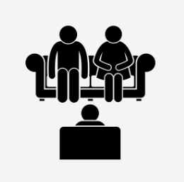 Two people sitting on a sofa with a person sitting in front of them.