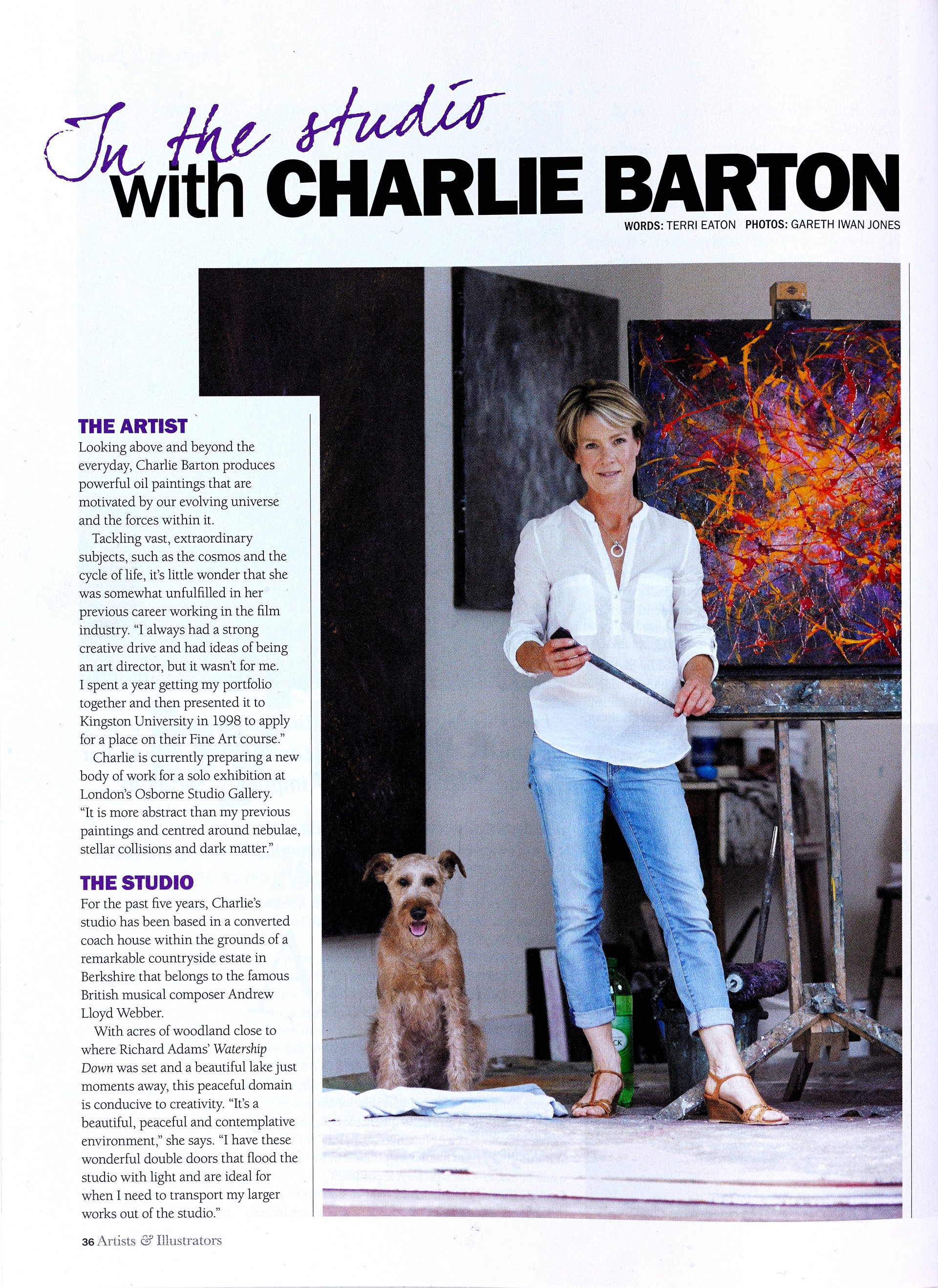 A woman with short blonde hair wearing a white blouse and jeans standing in an art studio, holding a paintbrush, with a colorful abstract painting behind her and a dog sitting on a white cloth on the floor.