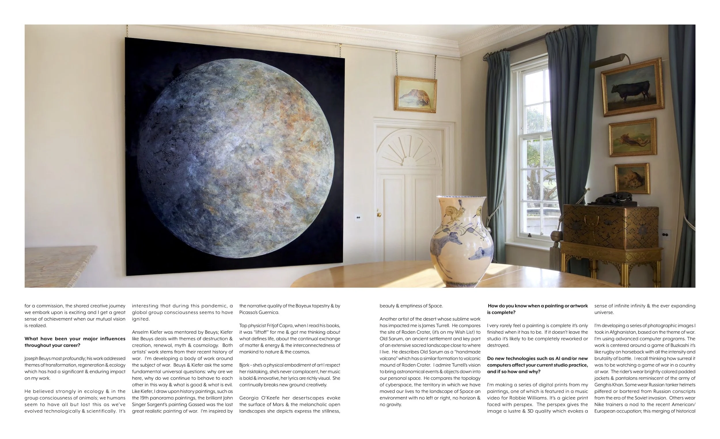 A large circular moon painting hanging on a white wall in a room with windows and blue curtains, with a decorative vase on a wooden table in the foreground and framed animal sketches on the wall.