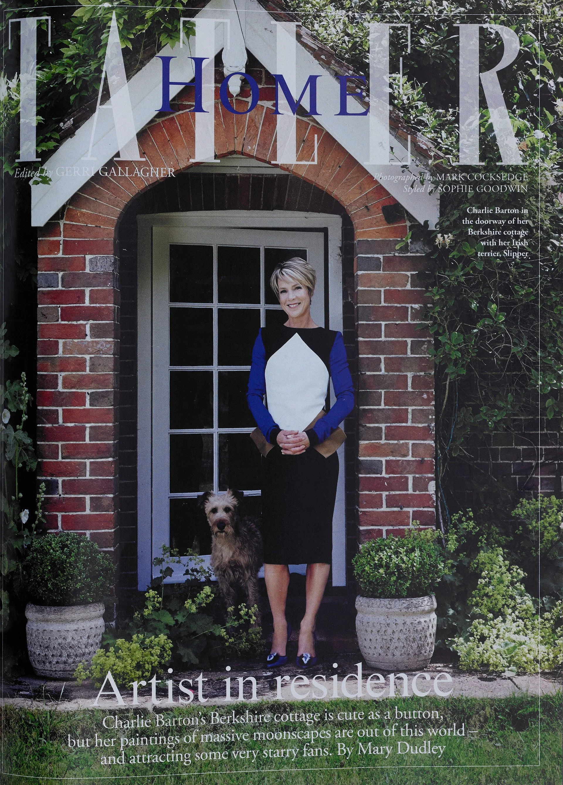 A woman standing in front of a brick doorway with a small dog, surrounded by potted plants and greenery, on the cover of a magazine titled 'HOME' with the subtitle 'Artist in residence.'