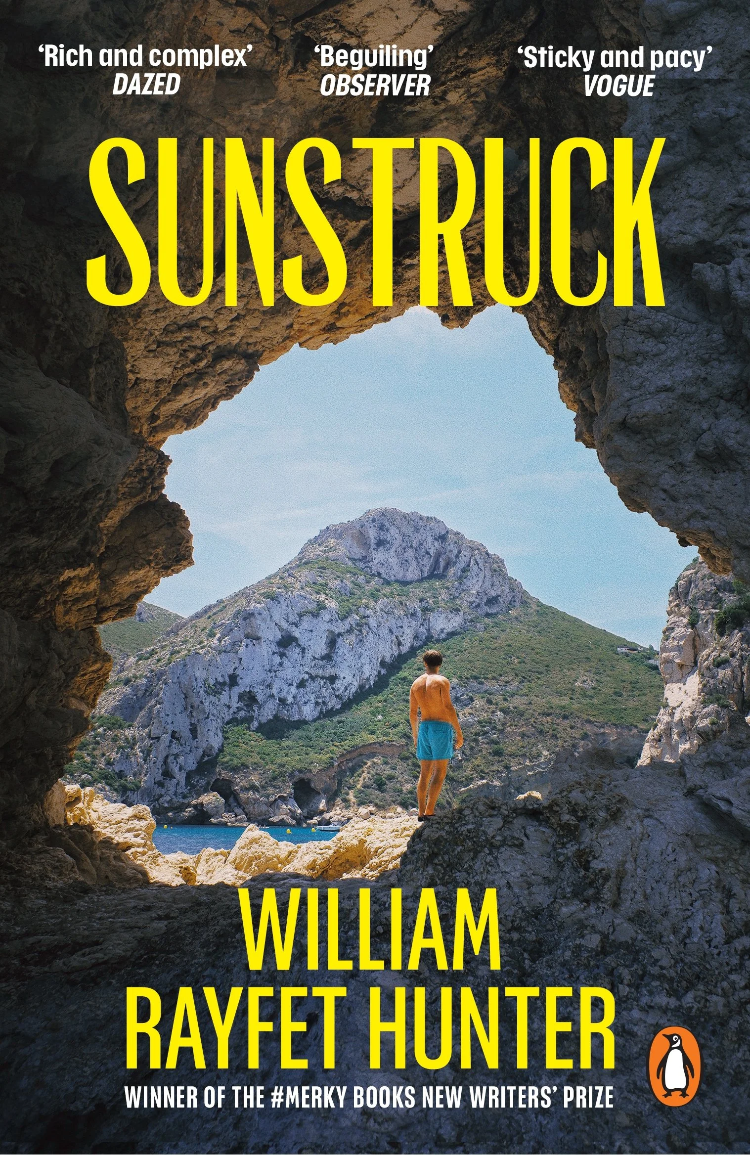 A man in orange shorts and a tank top stands on rocks overlooking a body of water, mountains, and a blue sky through a natural rock arch. The image features bold yellow text with quotes praising the book and names of authors William Davies and Rayfett Hunter, and includes quotes from Dazed, Observer, and Vogue. The Penguin logo is at the bottom right corner.
