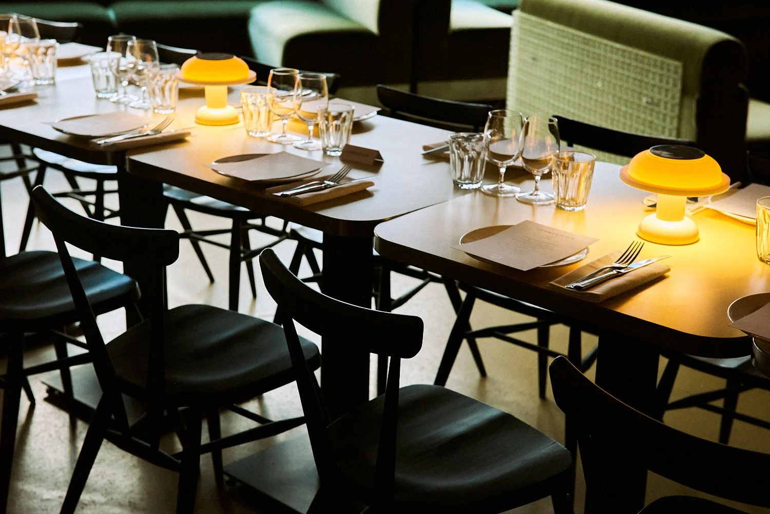 A dimly lit restaurant table set with glassware, plates, and cutlery, featuring two yellow lamps as centerpieces.
