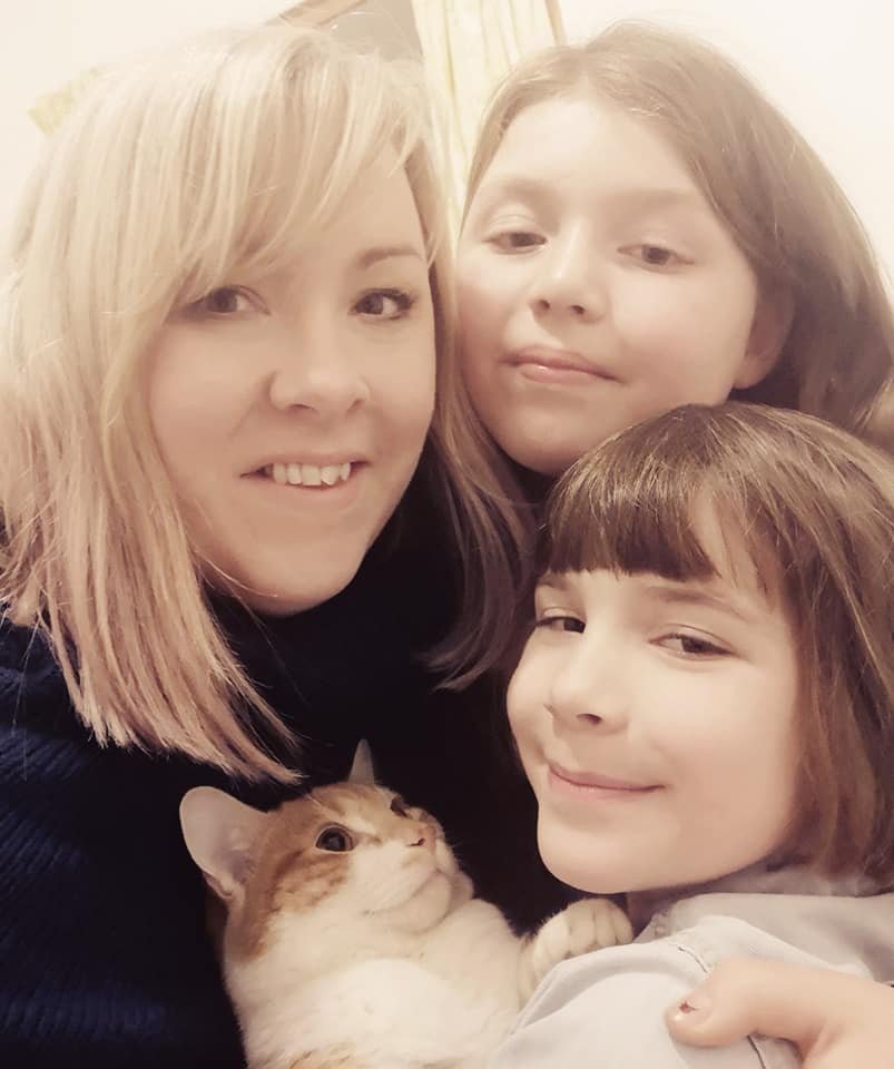 Three women with light skin and a cat posing for a selfie.