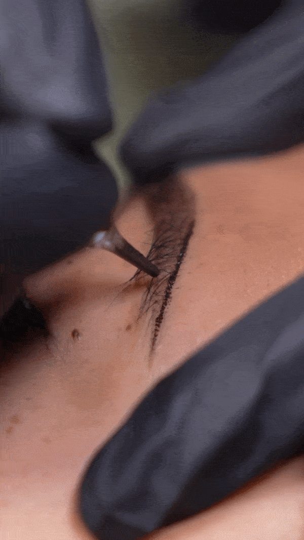 Close-up of a person drawing a tattoo on skin with a tattoo machine.