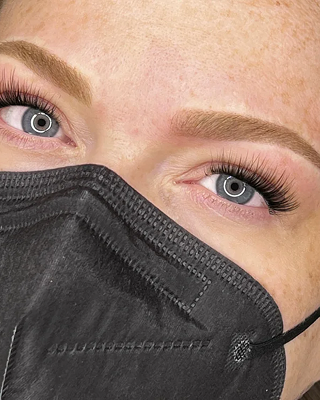 Close-up of a woman's eyes and eyebrows, wearing a black face mask.