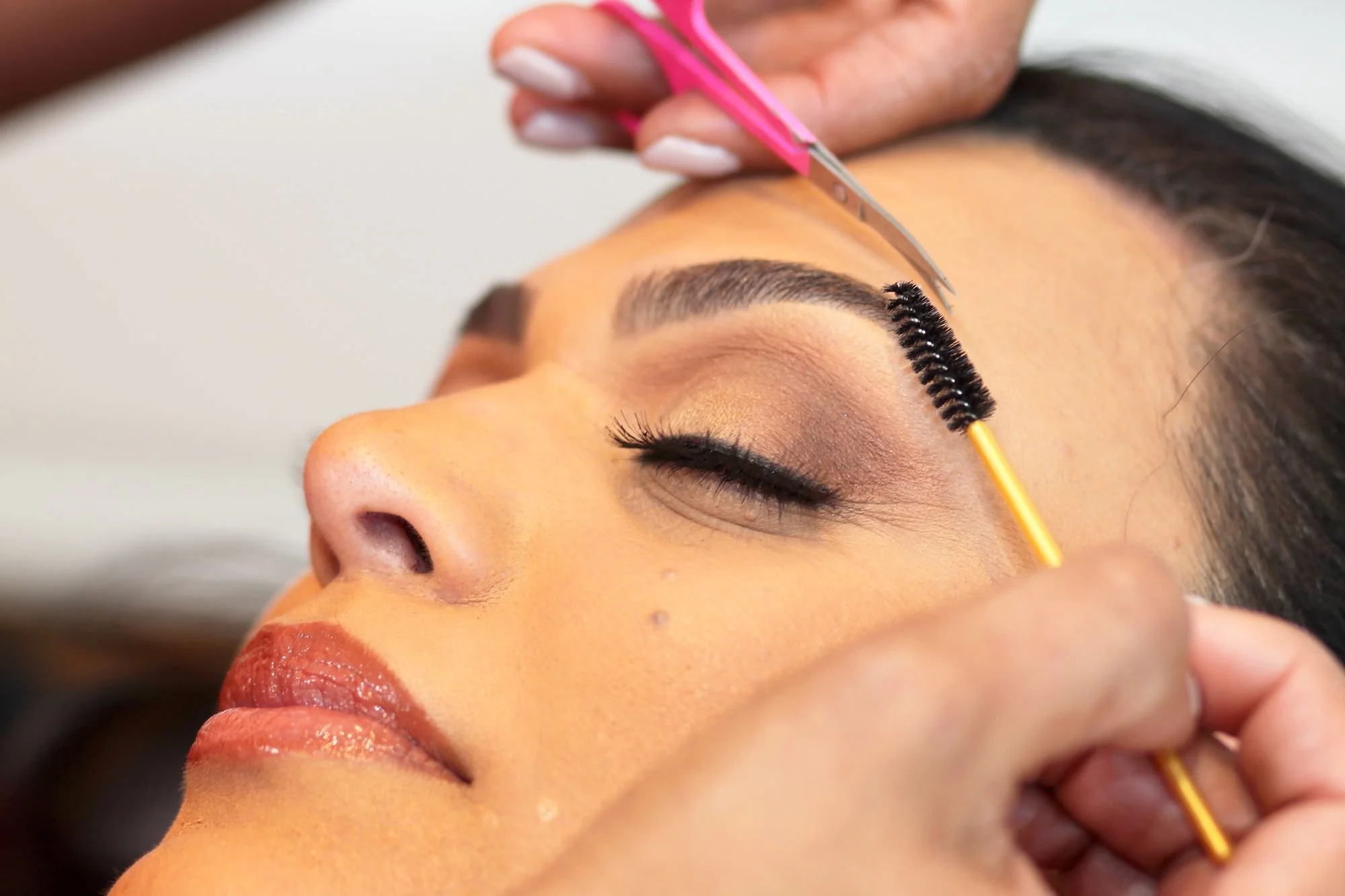 Close-up of a woman receiving eyelash extensions at a beauty salon, with a technician using tweezers to apply individual lashes.