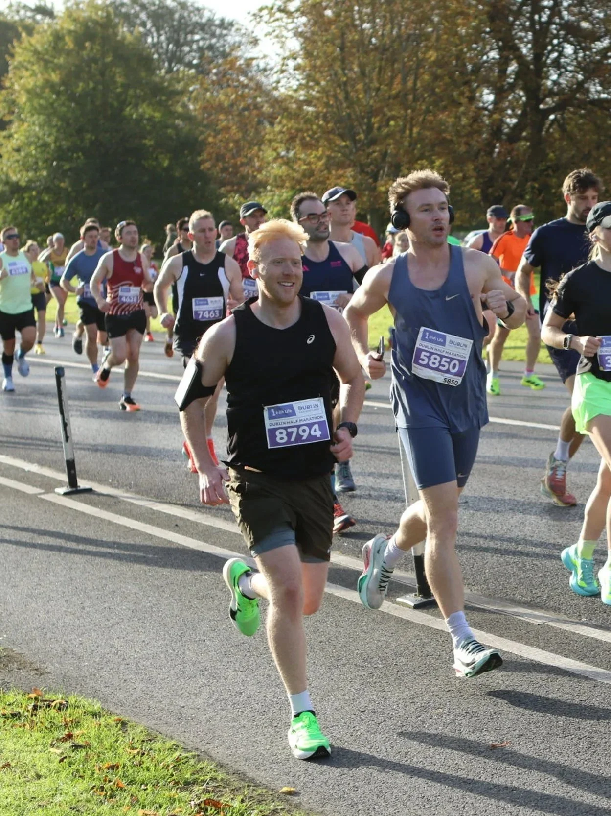 Marathon runners participating in a race on a paved road with trees in the background, wearing athletic clothing and numbered bibs.
