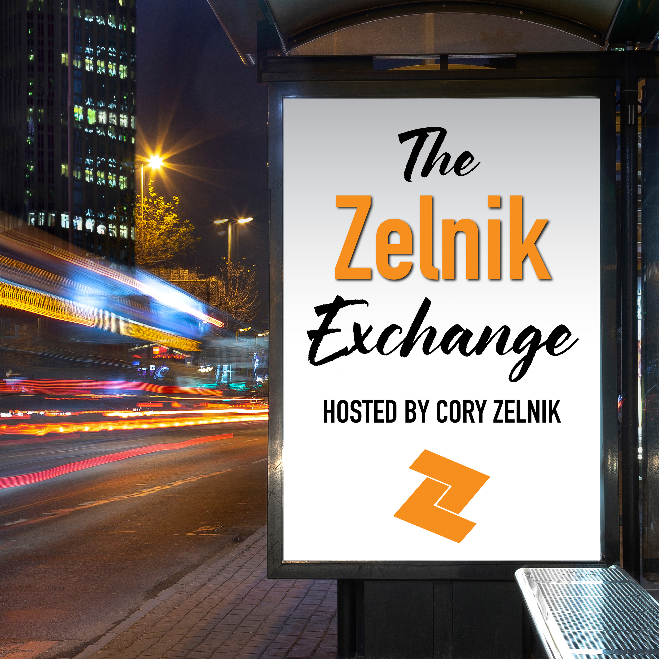 Night scene at a bus stop with a white sign displaying black and orange text that reads 'The Zelk'. The bus stop is located on a city street with high-rise buildings illuminated in the background. Light trails from moving vehicles are visible on the street.