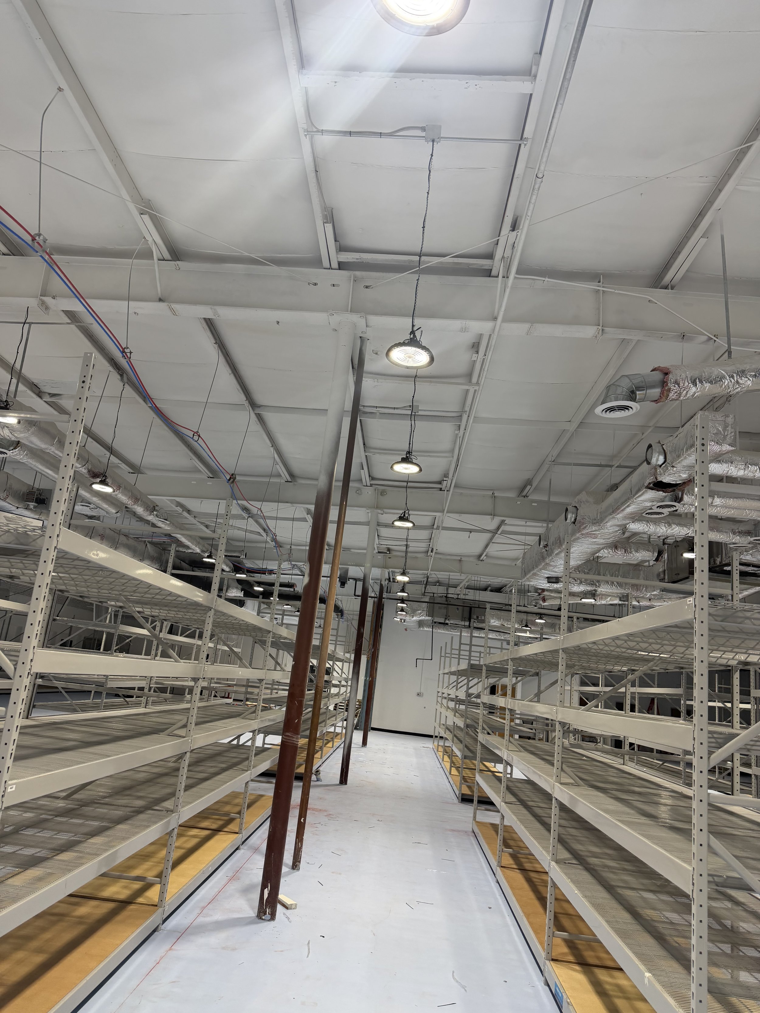 Empty retail shelves in an industrial store with exposed ductwork and lighting.