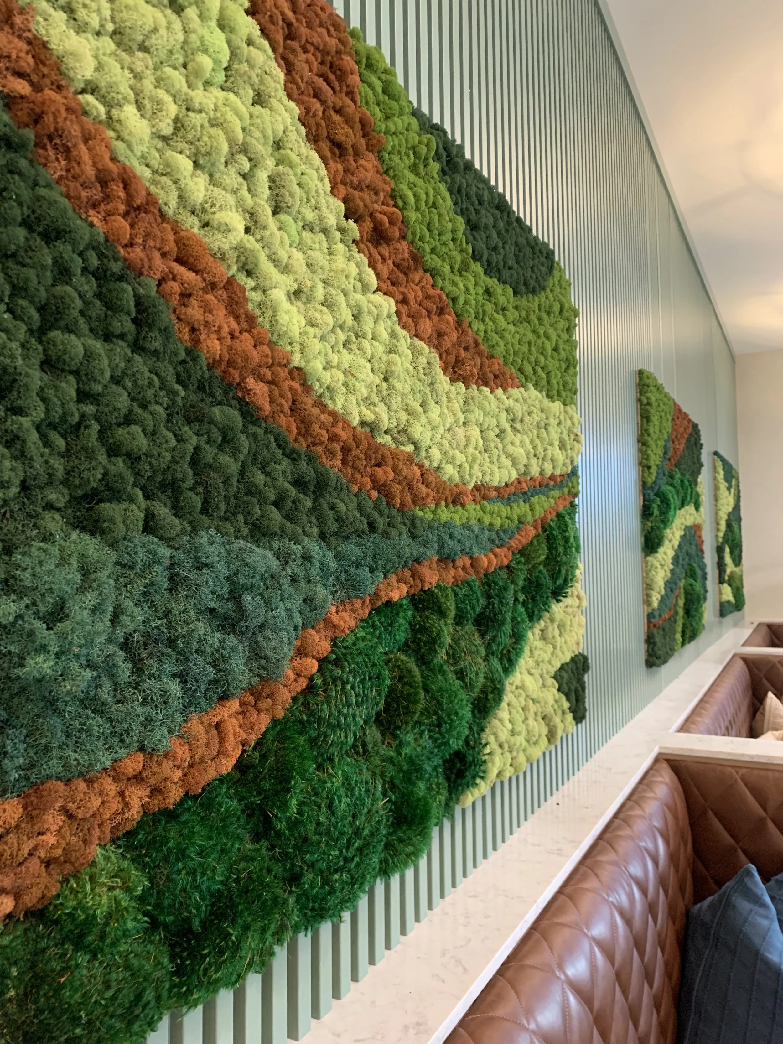 Decorative wall made of colorful moss arranged in patterns, with vertical light green slats and brown leather seating below.