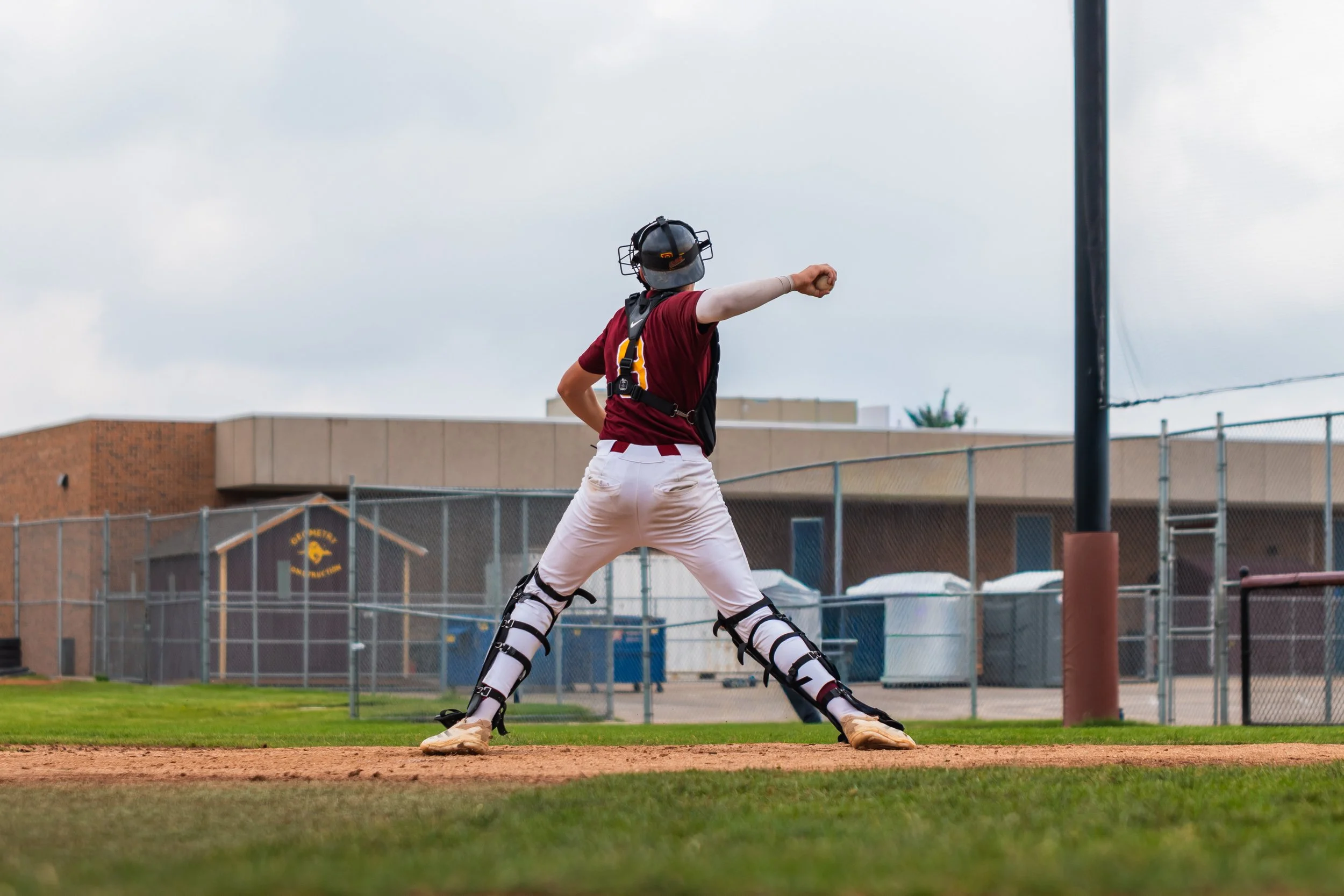 A baseball catcher in uniform with protective gear preparing behind home plate on a baseball field.