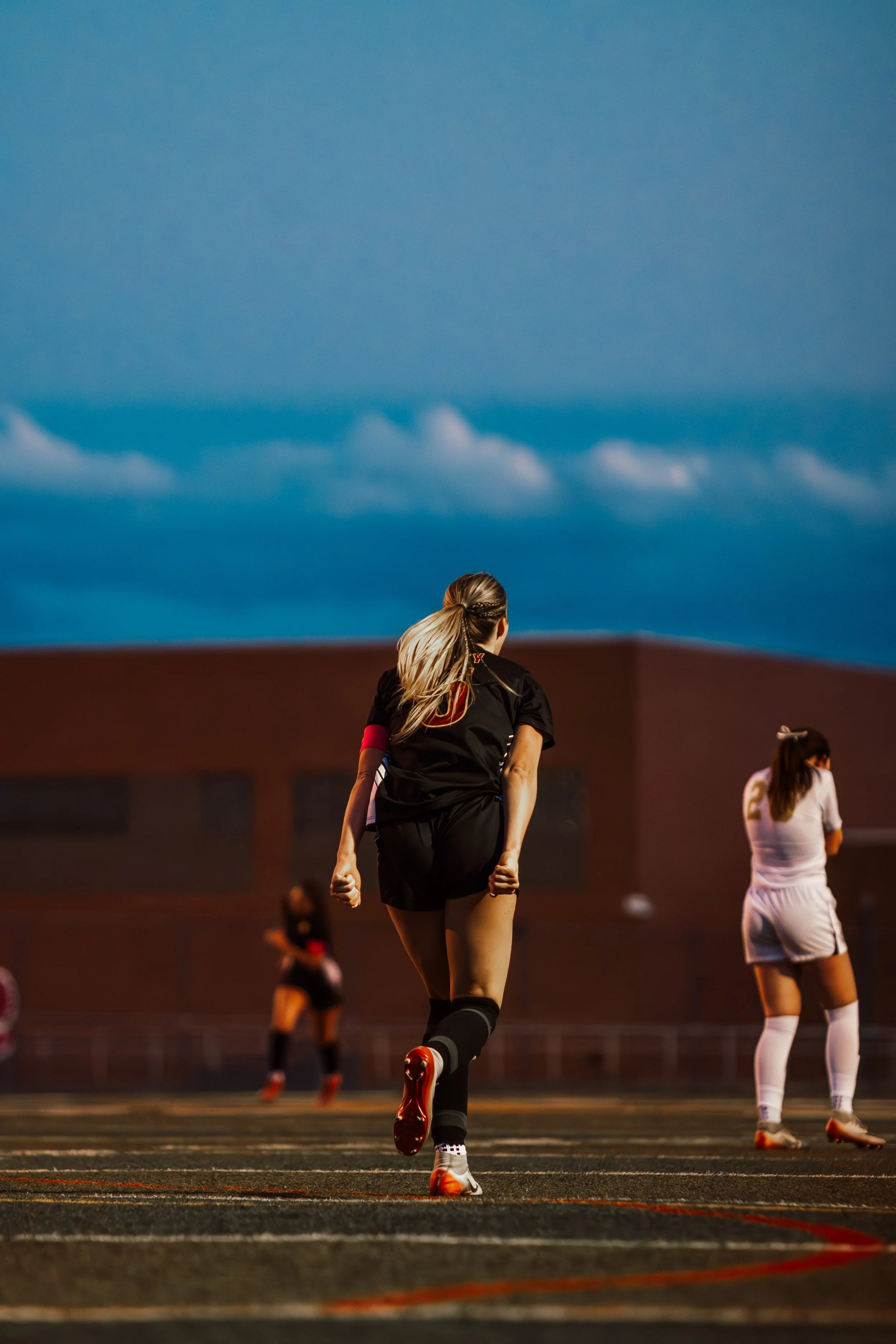 A group of female soccer players on a field during a game at dusk, with a clear blue sky overhead.