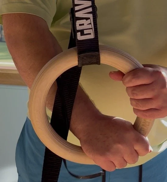 Person holding gymnastics rings with one hand, close-up of arms and rings.