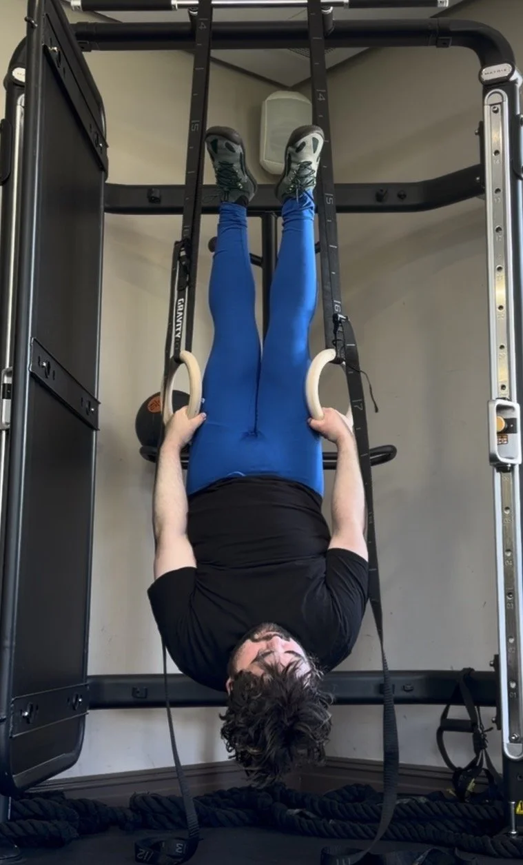 Person performing inverted exercise using gymnastic rings attached to a power rack in a home gym.
