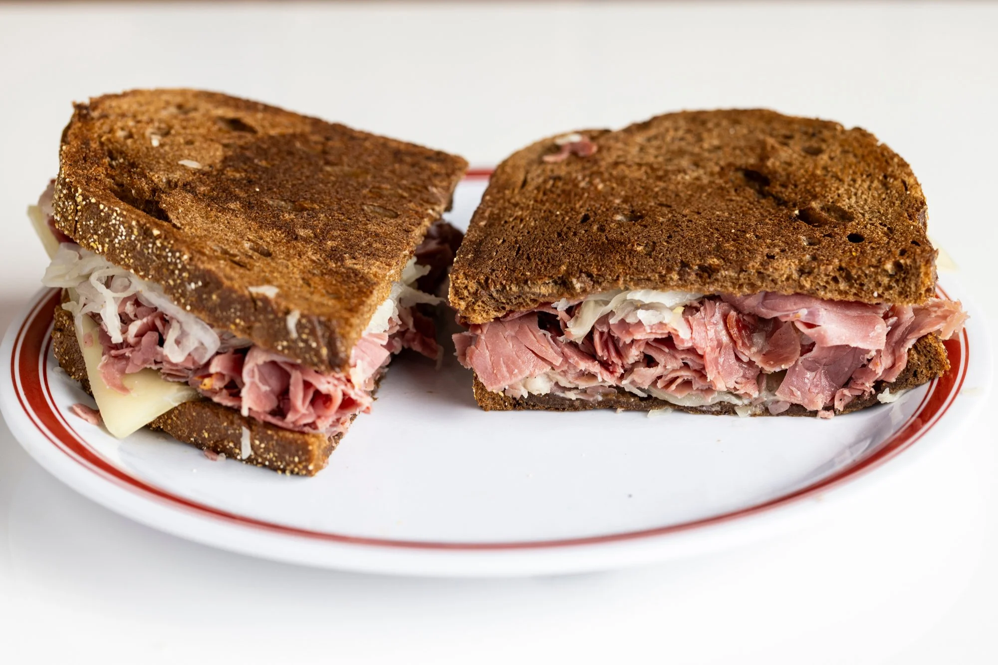 Close-up of a Reuben sandwich cut in half showing corned beef, sauerkraut, and Swiss cheese between slices of rye bread on a white plate.