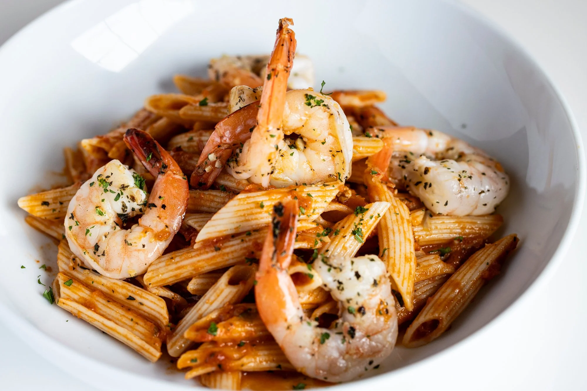 A bowl of seafood pasta with shrimp and a tomato-based sauce, garnished with herbs.